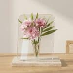 Sur une table lumineuse, le vase transparent carré en acrylique ressemble à un cadre clair rempli d’eau où une fleur semble flotter, créant un effet moderne et minimaliste.