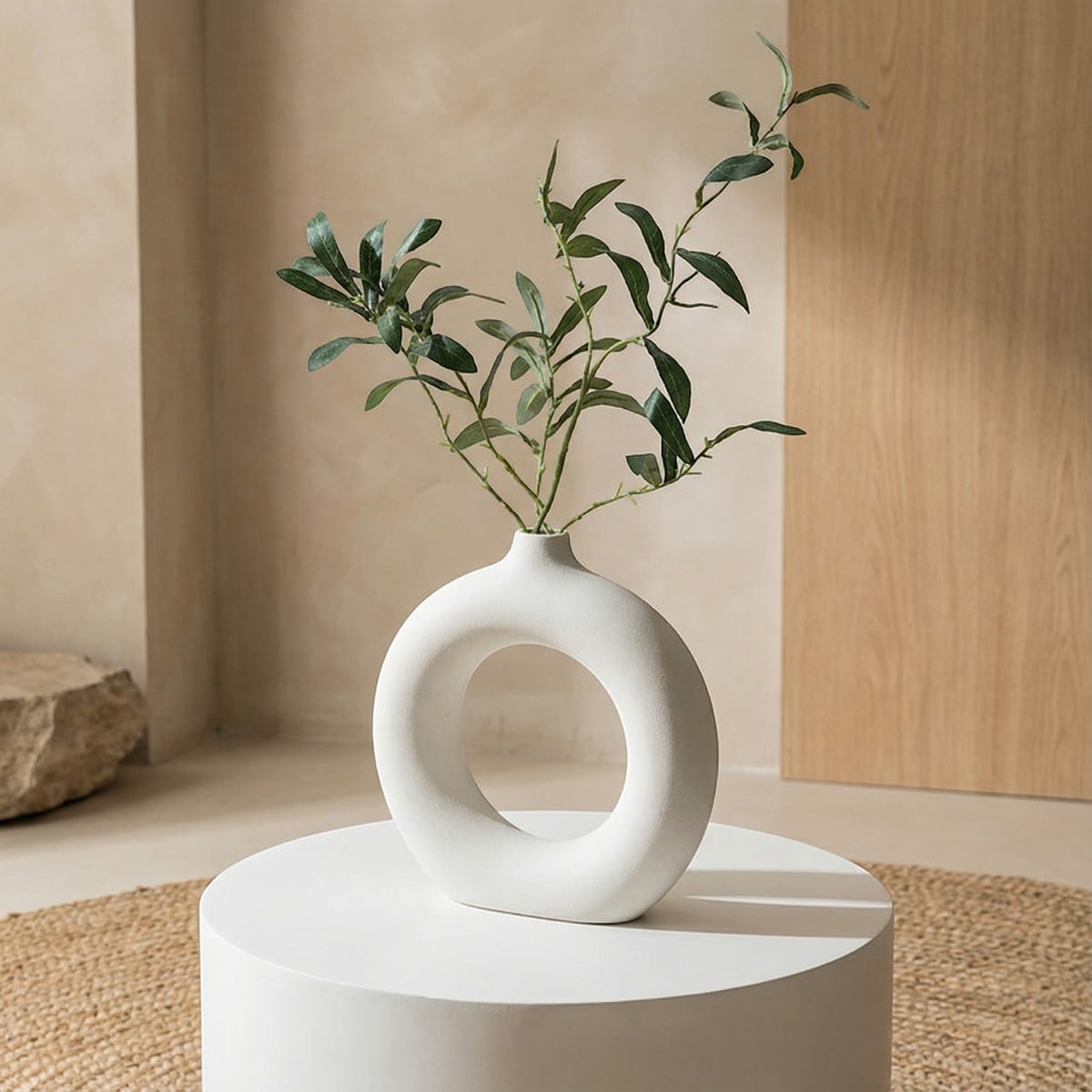 Pot décoratif minimaliste pour composition florale posé sur table bois clair : vase circulaire design japandi mat avec ouverture centrale, accueillant quelques tiges élégantes.