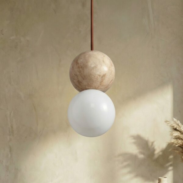Suspension japandi boule en pierre naturelle beige et verre dépoli blanc, deux sphères superposées, câble cuivré, étagère bois et vases beige en fond.