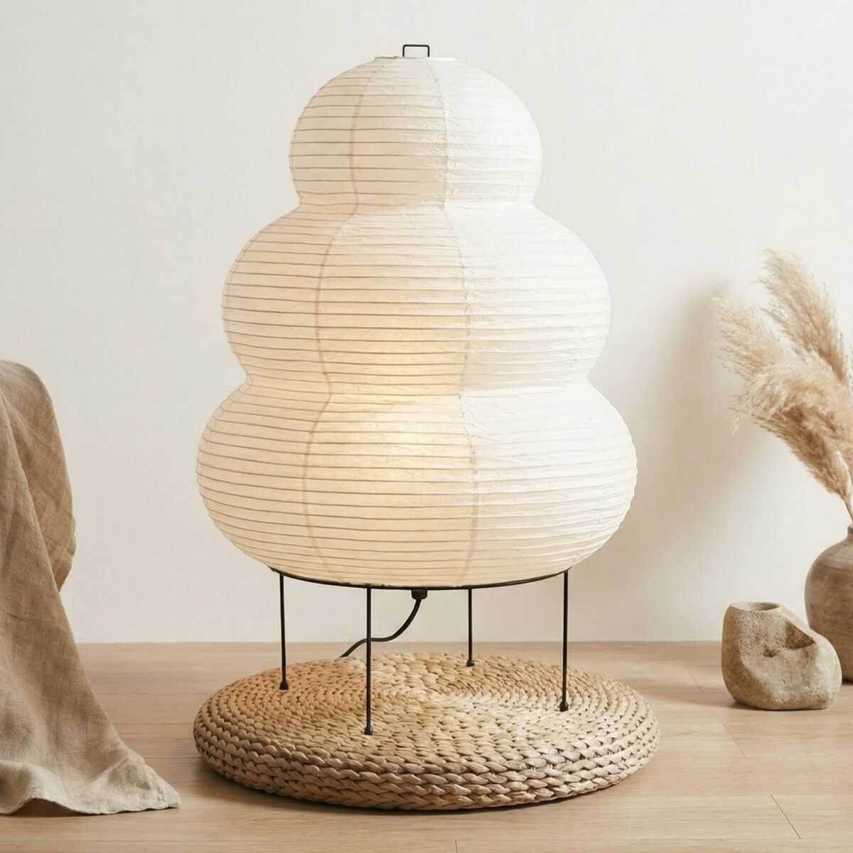 Lampadaire japandi en forme de gourde en papier et métal blanc posé sur natte en rotin parquet clair avec herbes de pampa et pierre brute.
