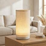 La lampe de table japandi cylindre blanc chaud USB posée sur un meuble en bois clair dans un salon minimaliste beige avec canapé et herbes de pampa.