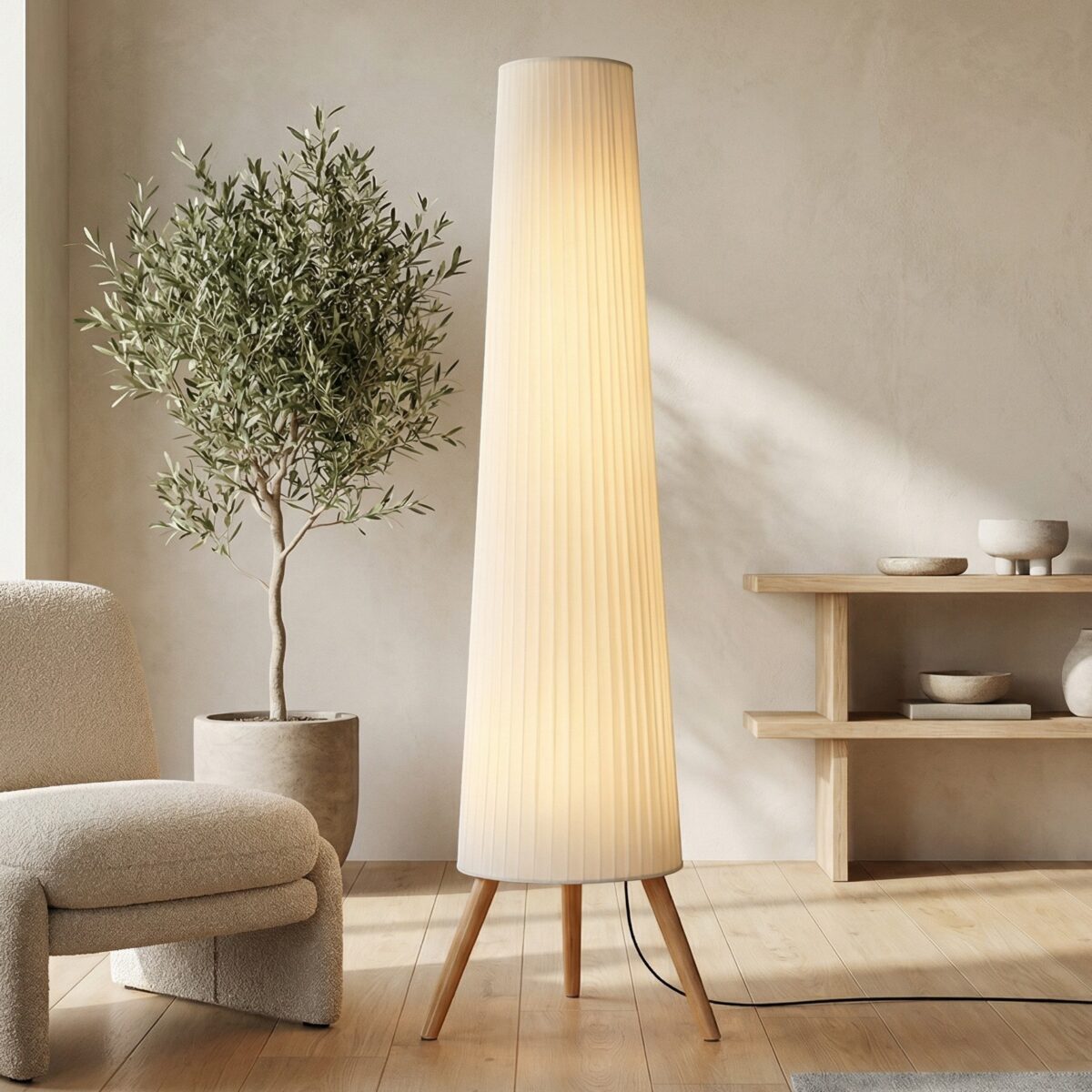 Lampadaire japandi abat-jour plissé et bois naturel sur trépied clair, posé dans un salon beige aux côtés d'un fauteuil bouclette et d'un olivier