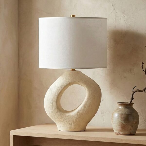 Lampe japandi en résine sculptée et abat-jour cylindrique posée sur console bois clair, base beige trou central effet pierre, lumière douce ambiance zen minimaliste.