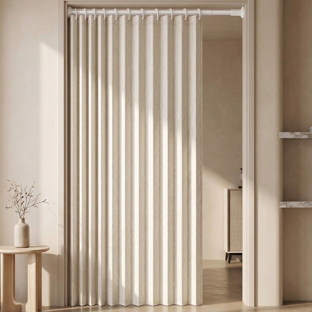 Dans une ouverture intérieure, le Rideau de porte japonais plissé esprit japandi épuré forme des plis verticaux élégants, filtrant la lumière et séparant deux pièces dans un décor minimaliste.