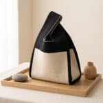 Mini sac kinchaku japonais tricot bicolore femme posé sur plateau bois, sac textile noir et beige à maille épaisse avec poignée pliée, style Japandi minimaliste élégant.