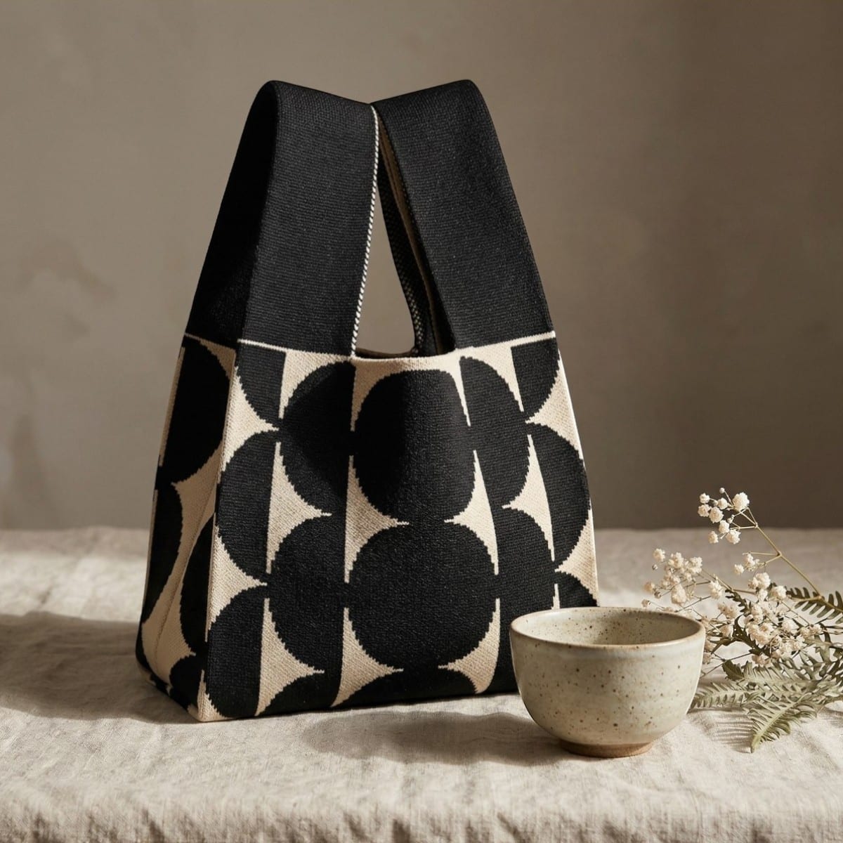 Sac japonais motif traditionnel minimaliste en maille tricotée noire et beige, sur une table couverte d'une nappe.