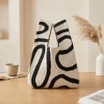 Sac japonais tricoté motif ondulé noir et écru : petit sac en maille épaisse avec motifs vagues contrastés noir et écru, posé sur une table en bois beige.