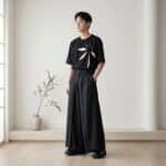 Un jeune homme asiatique portant le pantalon japonais hakama noir streetwear homme au style samue moderne de couleur noire et très large, accompagné d'un t-shirt blanc, dans une pièce épurée et lumineuse avec un vase décoratif.