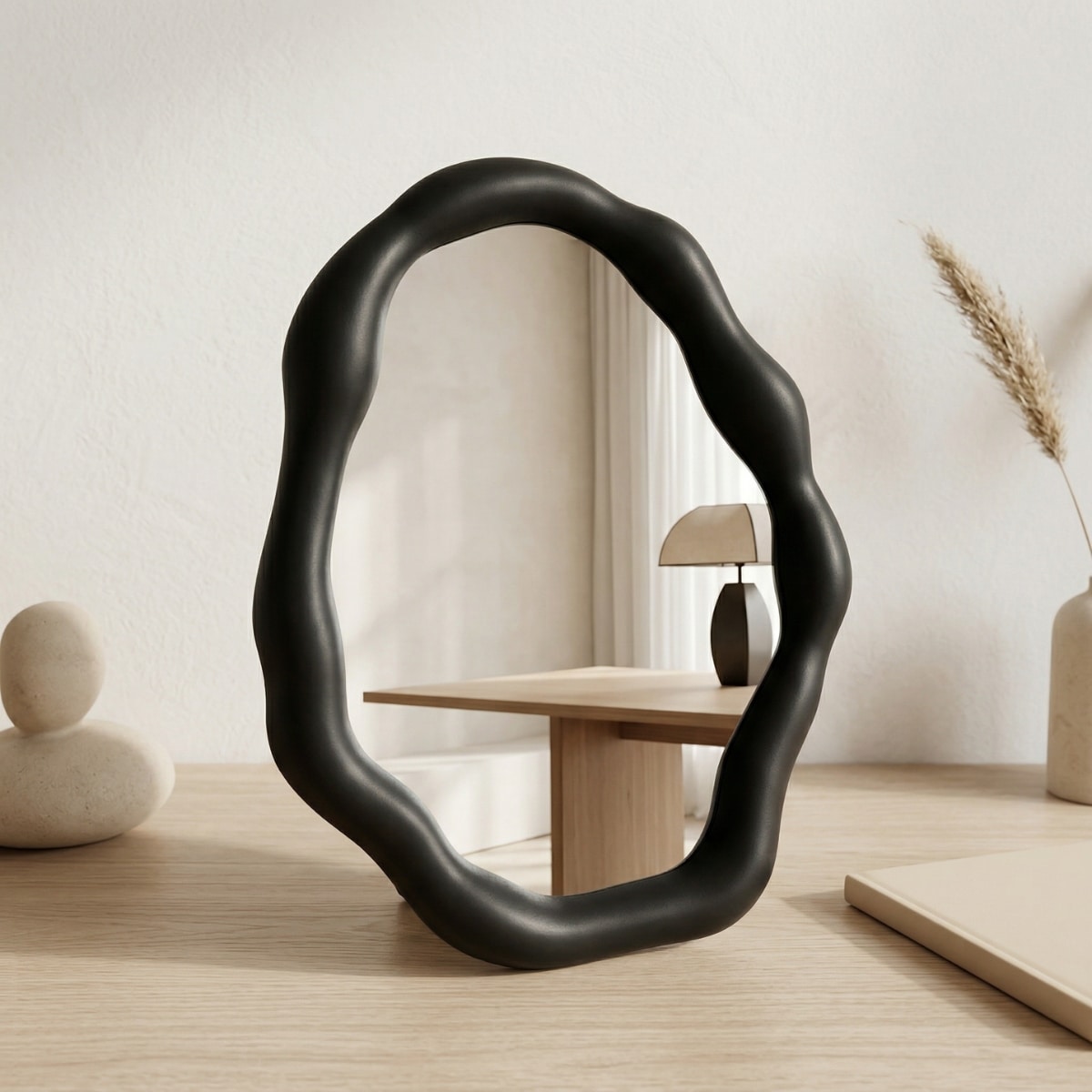 Petit miroir japandi forme organique style wabi-sabi, de couleur noir, posé sur une table beige