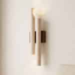 Applique murale double cylindre Japandi en travertin beige poreux fixée sur support bois brun foncé, diffusant un halo lumineux vers le haut sur mur crème.