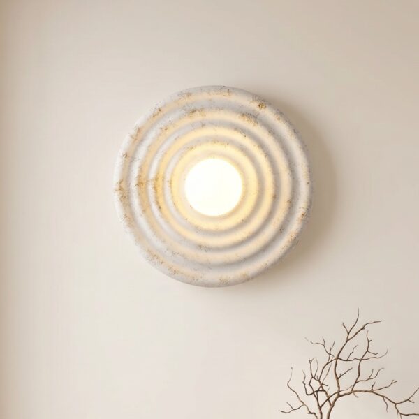 L'applique murale ronde japandi effet ondule en résine, blanche avec reflet doré sur un mur beige.