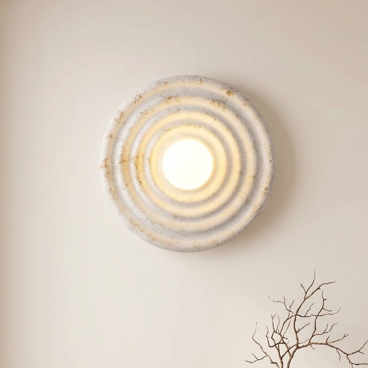L'applique murale ronde japandi effet ondule en résine, blanche avec reflet doré sur un mur beige.