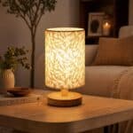 La lampe de table japandi abat-jour géométrique doré base bois cylindrique allumée sur table en bois, motifs triangles dorés rétroéclairés, salon chaleureux en fond.