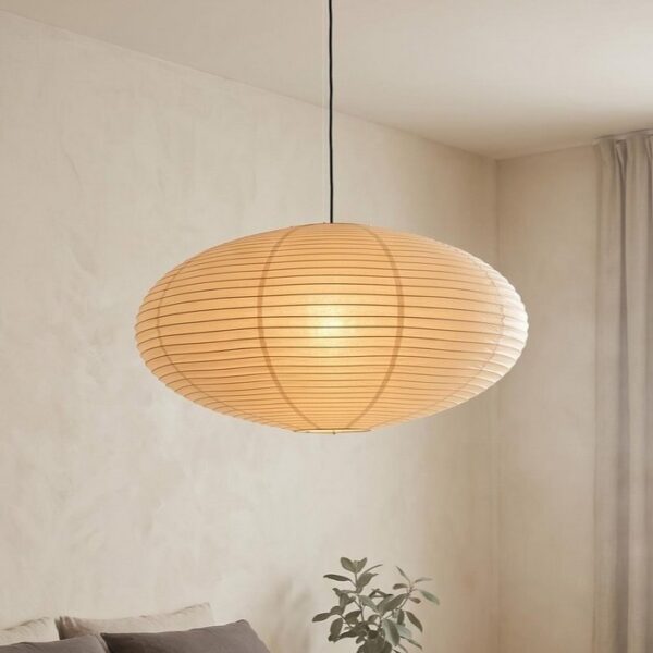 Suspension ellipse papier Japandi naturel beige aplatie à nervures horizontales, suspendue par câble noir dans un salon aux murs blancs et rideaux clairs.