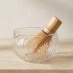 Bol japonais pour matcha en verre transparent texturé, avec un fouet pour matcha, posé sur une table beige