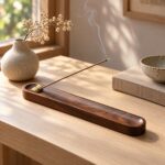 Un porte-encens japonais en bois de noyer à embout réglable, posé sur une table avec un bâton d’encens fumant, dans un intérieur chaleureux et lumineux.
