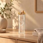 Un porte-encens japonais colonne de verre pour bâtons et cônes, posé sur un meuble en bois, avec un bâton d’encens allumé et sa fumée, dans un intérieur chaleureux.