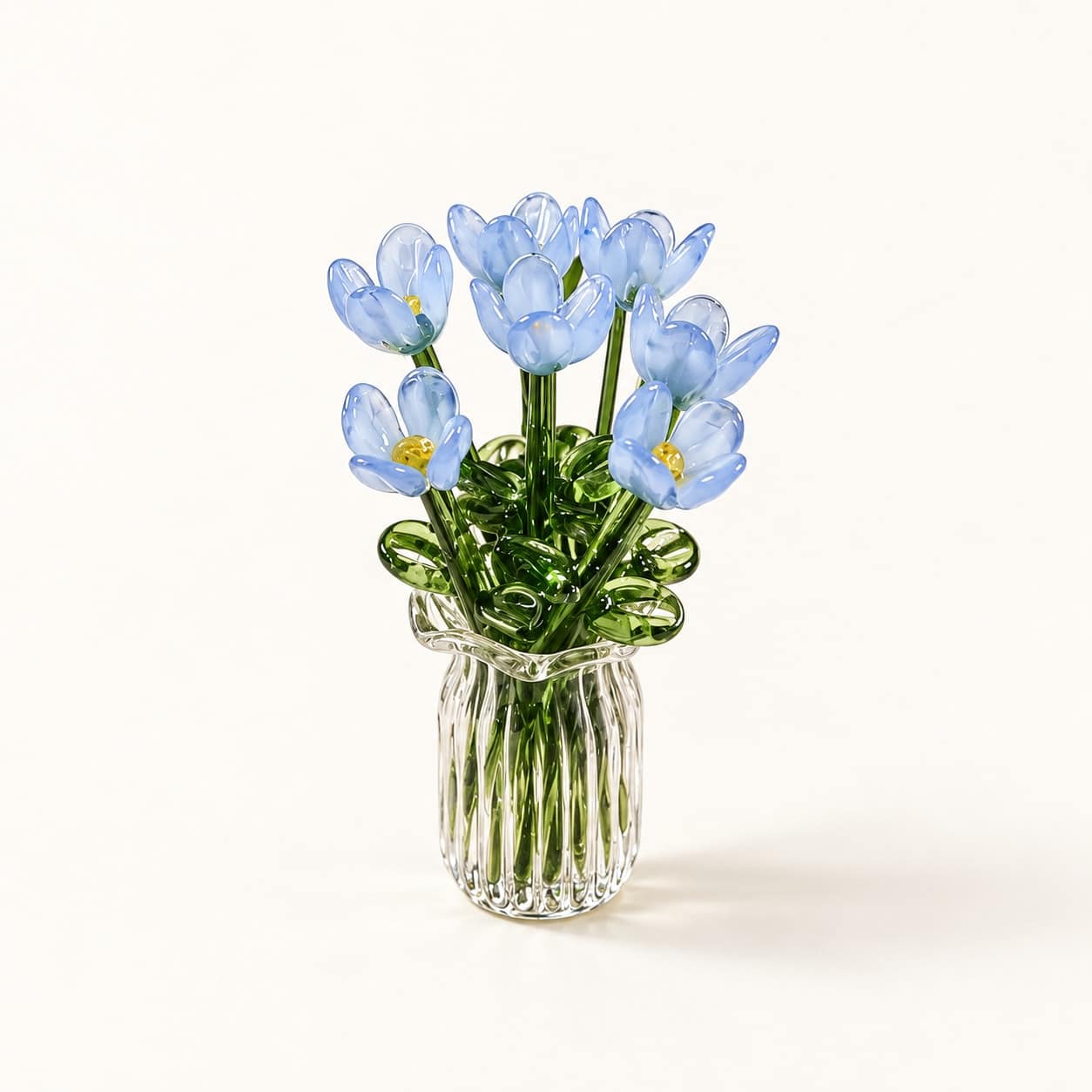 Mini bouquet bleu en verre et vase transparent strié sur fond crème